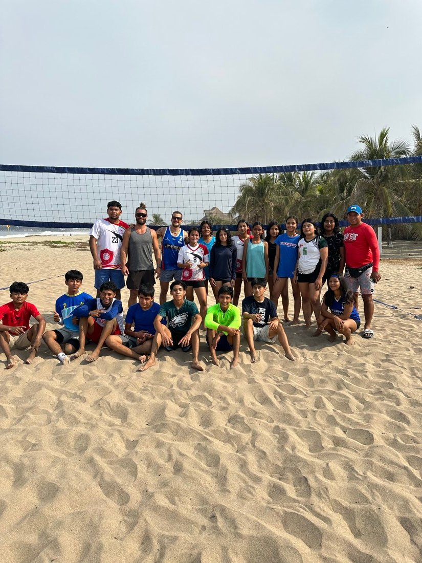 A group of players and coaches together at the net after a beach session in Puerto Escondido.