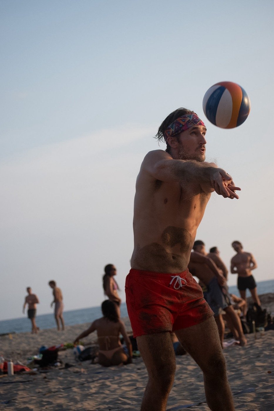 A player mid forearm-pass, ball in the air, beach behind.