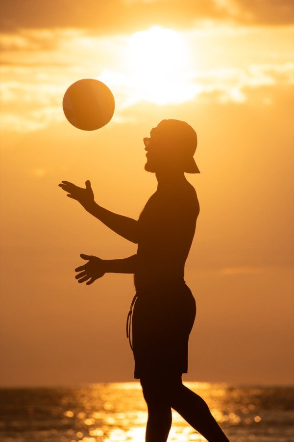 A player tossing the ball to serve, silhouetted at sunset.