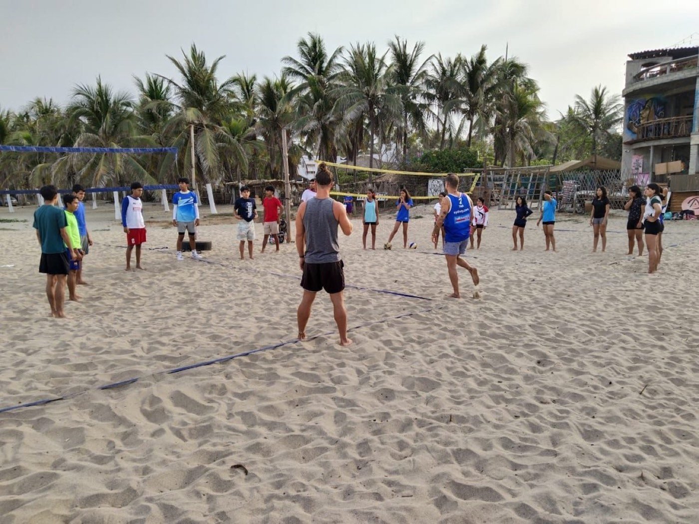 A training session on the beach courts, ocean and palms behind.