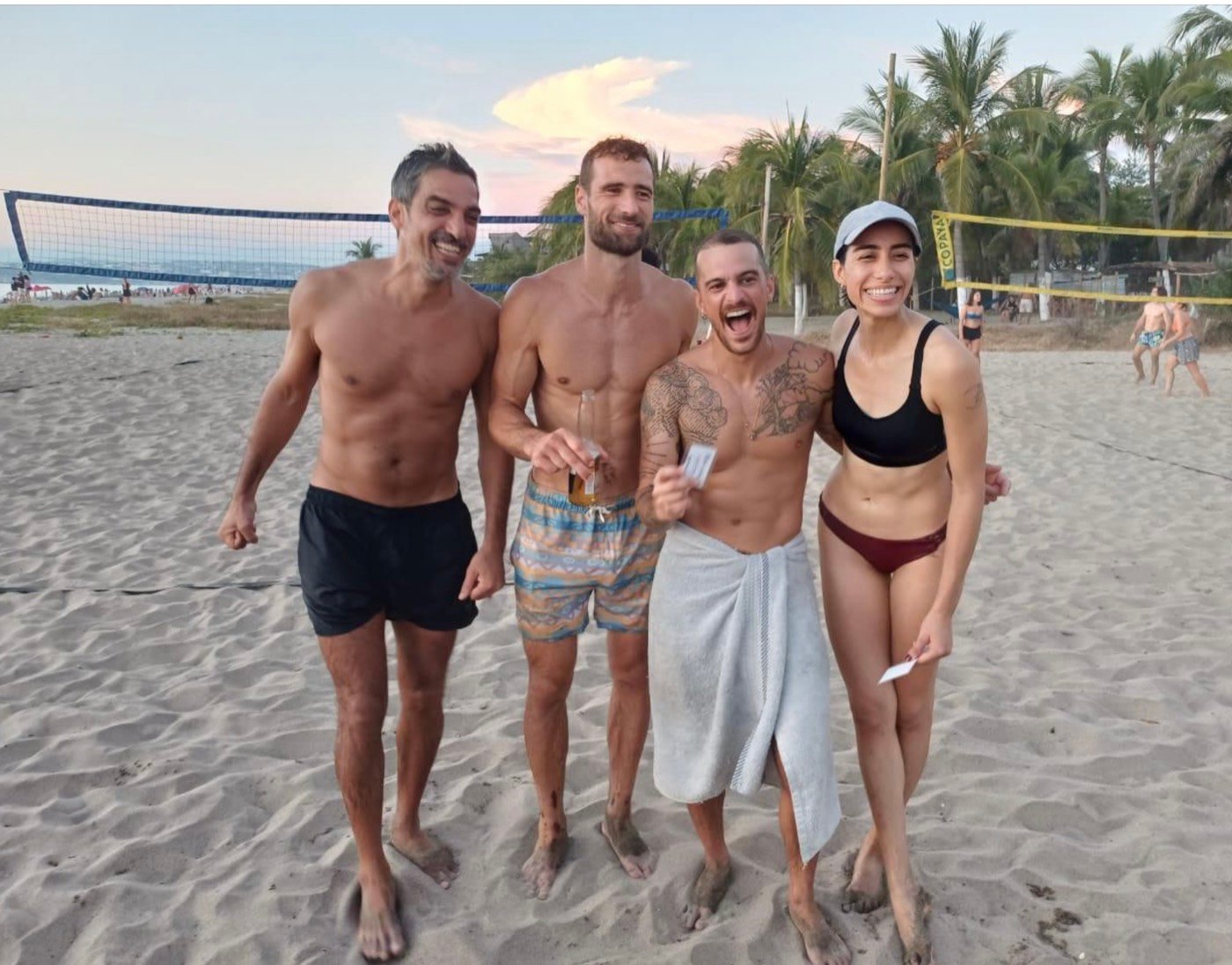 A diverse group of four players and coaches together on the beach at golden hour.